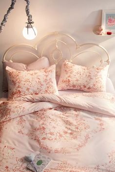 a bed with pink and white comforters in a bedroom next to a wall light