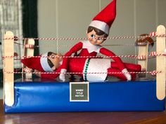 an elf sitting on top of a blue box next to a red and white striped rope