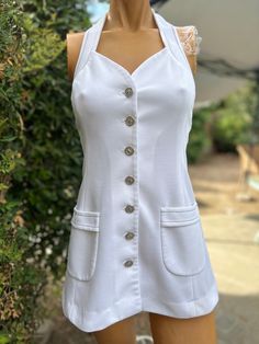 Here is a vintage 1970s white halter polyester tennis dress.Made by Top Seed. Following are the measurements. Bust 32",Waist 28",Hips 38".Made out of a white polyester fabric.Buttons down the front and neck with silver cross buttons. Navy blue top stitching. In nice vintage condition. Please take special consideration of measurements. 1970 sizing was much smaller than today's standards. Take extra special note of length. Tennis dresss were very short not like a regular dress.If you live overseas please email me first before purchasing for mailing cost. Price quoted is for USA only White Vintage A-line Mini Dress, White Lined Halter Neck Mini Dress, Vintage White Mini Dress For Summer, Vintage White Summer Mini Dress, White Halter Neck Mini Dress Lined, White Retro Dress With Buttons, White Halter Neck Lined Mini Dress, Vintage White Halter Neck Dress, White Retro Mini Dress For Summer