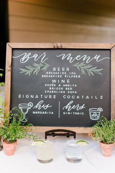 a chalkboard sign that says bar menu with plants and drinks on the table next to it