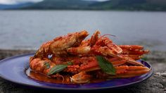 a blue plate topped with cooked lobster next to a body of water and mountains in the background