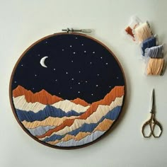 a pair of scissors and some thread on a table with an embroidery project in the shape of mountains