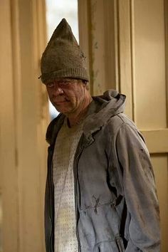 an old man wearing a hat standing in front of a door