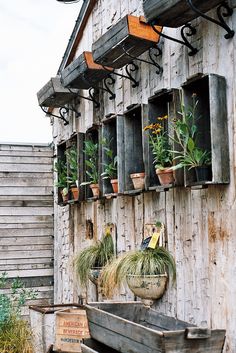 an old wooden building with potted plants on the windows sill and hanging planters