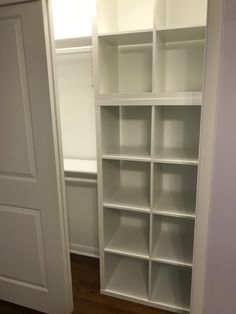 an empty white bookcase in the corner of a room with wooden floors and doors