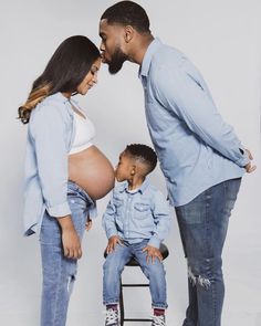 an image of a pregnant woman and her husband kissing their son's belly while he sits on a chair