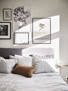 a bed with white sheets and pillows in front of pictures on the wall above it