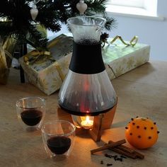 a table topped with two glasses and a vase filled with liquid next to a christmas tree