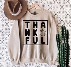 a sweater with the words thinkful on it next to a cactus