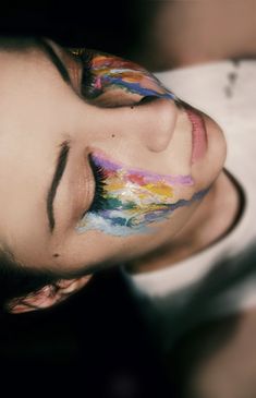 a woman with her face painted like a rainbow and looking up at the camera while she has her eyes closed