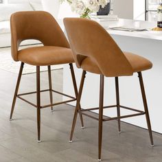 two brown bar stools sitting next to each other in front of a kitchen counter