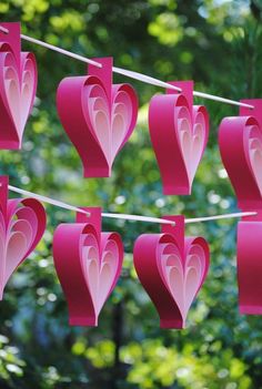 pink paper hearts hanging from a line in front of some green trees with leaves on them