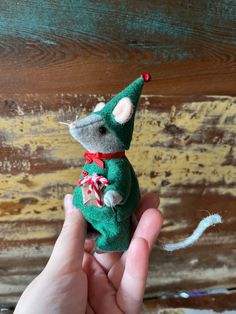 a hand is holding a small green toy mouse with a red ribbon around its neck