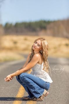 a woman kneeling down on the side of a road with her hand on her hip