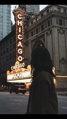 a woman standing in front of the chicago theater marquee at dusk with her back turned to the camera