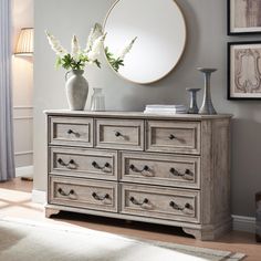 a white vase with flowers sitting on top of a wooden dresser next to a mirror