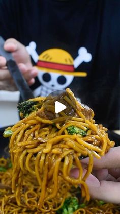 someone is holding up some noodles with broccoli and other things in the background