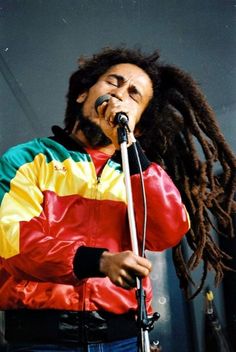 a man with dreadlocks on his head singing into a microphone and wearing a colorful jacket