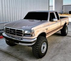 a truck parked in front of a building with large tires on it's rims