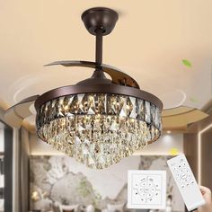 a person holding a remote control in front of a ceiling fan with a chandelier