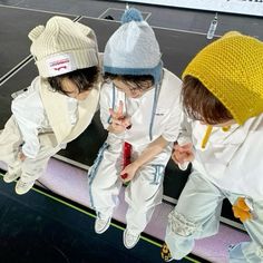 three young children wearing white clothing and knitted hats on top of a tennis court