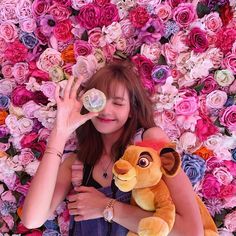 a woman holding a stuffed animal in front of a flower wall