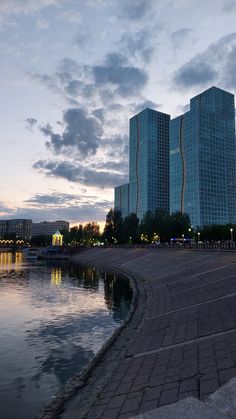 two tall buildings next to a body of water at dusk with clouds in the sky