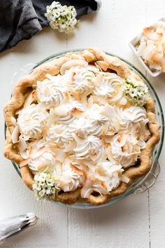 a pie topped with whipped cream and flowers on top of a white table next to silverware