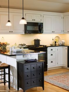 a kitchen with white cabinets and black counter tops is lit by two pendant lights above the island