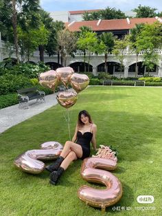 a woman sitting in the grass with some balloons and letters that spell out her name