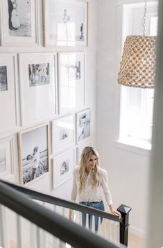 a woman standing on the stairs in front of many framed pictures and a chandelier