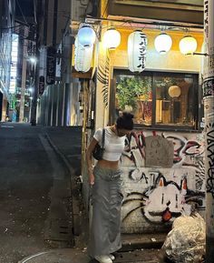 a woman standing on the side of a street next to a building covered in graffiti