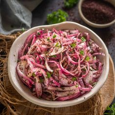 a white bowl filled with red onions on top of a wooden table next to some herbs