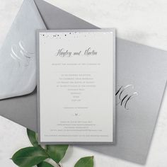 an elegant wedding card with silver foil on the front and back, sitting next to a green leafy branch