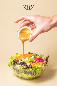 a hand pouring dressing into a salad with lettuce, carrots and other vegetables