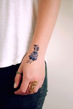 a woman's hand with a tattoo on her left wrist and gold ring in the middle