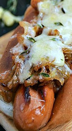 two hotdogs covered in cheese and onions on a wooden board with other food items