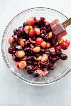 a bowl filled with cherries and nuts on top of a white table next to a wooden spoon