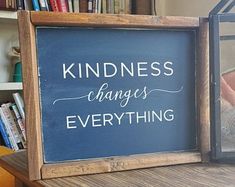 a sign that says kindness changes everything on it next to a book shelf filled with books