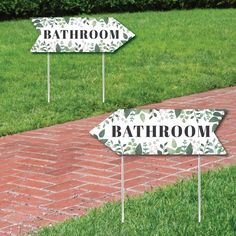 two signs that say bathroom and one has leaves on them in front of some grass