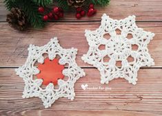 two crocheted snowflakes sitting on top of a wooden table next to pine cones