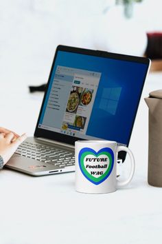 a laptop computer sitting on top of a table next to a coffee cup and mug