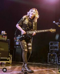 a woman in tights and boots playing an electric guitar on stage with a microphone