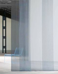 a blue chair sitting in front of a white wall with vertical blinds on it's sides