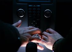 two hands are touching the buttons on a car's control panel in the dark