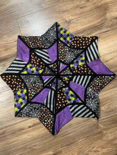 a purple, black and white patchwork quilted star on the floor with wood floors