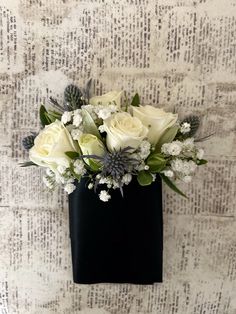 white roses and greenery in a black vase on a wallpapered background with text