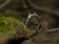 a silver ring with a red stone in the middle sitting on top of moss covered rocks