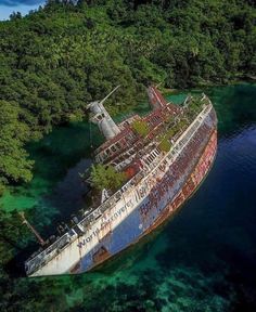 an old rusted ship in the ocean surrounded by green trees and blue water, from above