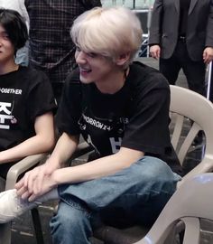 two young men sitting next to each other on chairs in front of a group of people